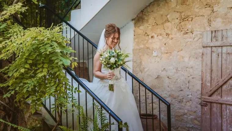 Hannah smiling and descending a garden staircase with her bouquet