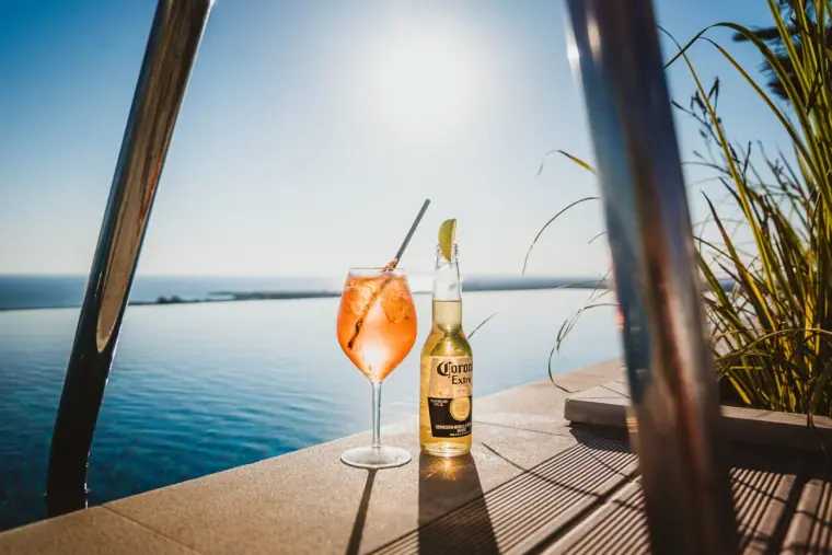 A cocktail and a bottle of beer on the poolside ledge at Napa Suites at sunset, sea behind