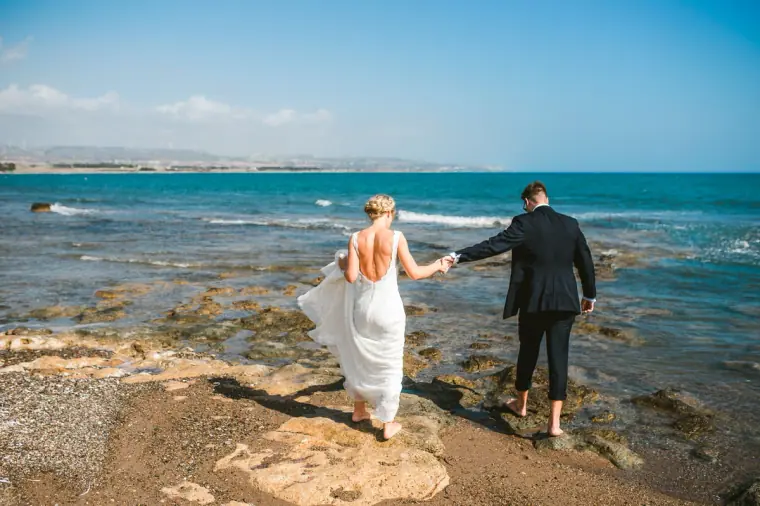 Rachel and Chris walking hand in hand along the rocky shore at Pissouri