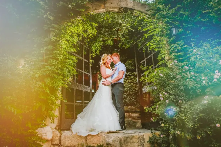 Bride and groom holding each other in the leafy stone doorway of Vasilias Nikoklis Inn, warm light flare