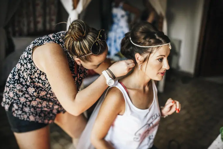 Bride in a pearl headpiece having her hair finished by a friend