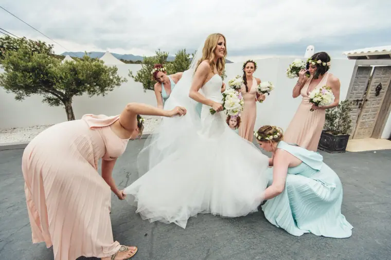 Bridesmaids in pastel dresses fluffing out the bride's gown