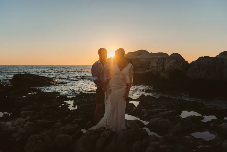Alana and Luke silhouetted against the setting sun on the rocks by the sea