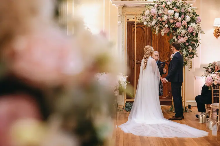 Ian and Jade exchanging vows beneath a lavish pink floral arch