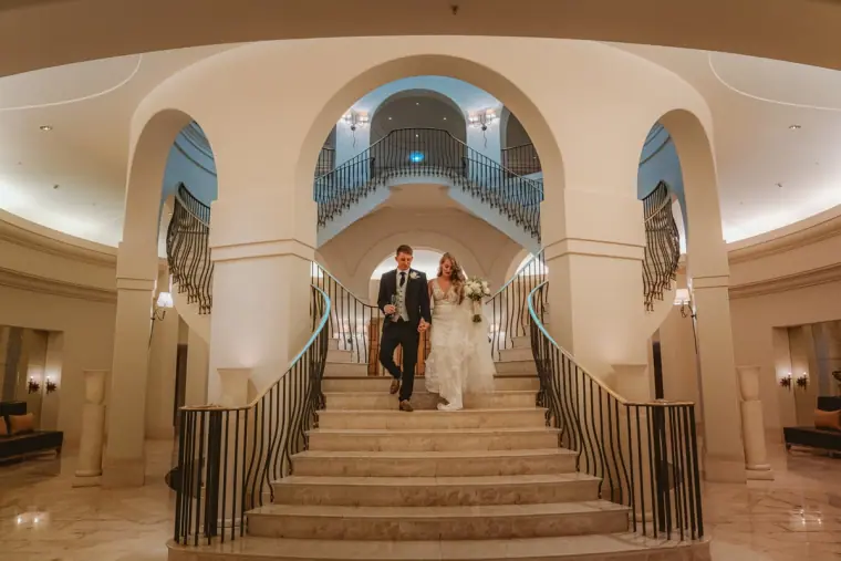Carly and Jack walking down the grand staircase inside Anassa Hotel