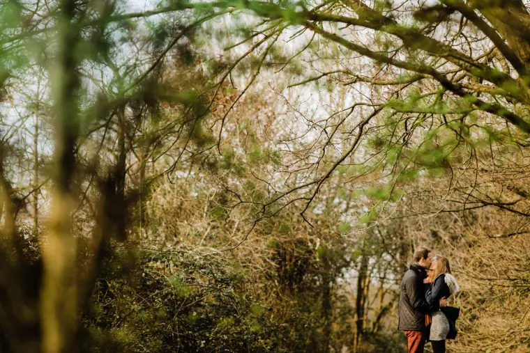 Couple standing together in the distance amid a tangle of woodland