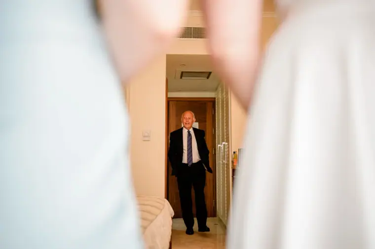 Bride's father in a suit glimpsed through a doorway before seeing her