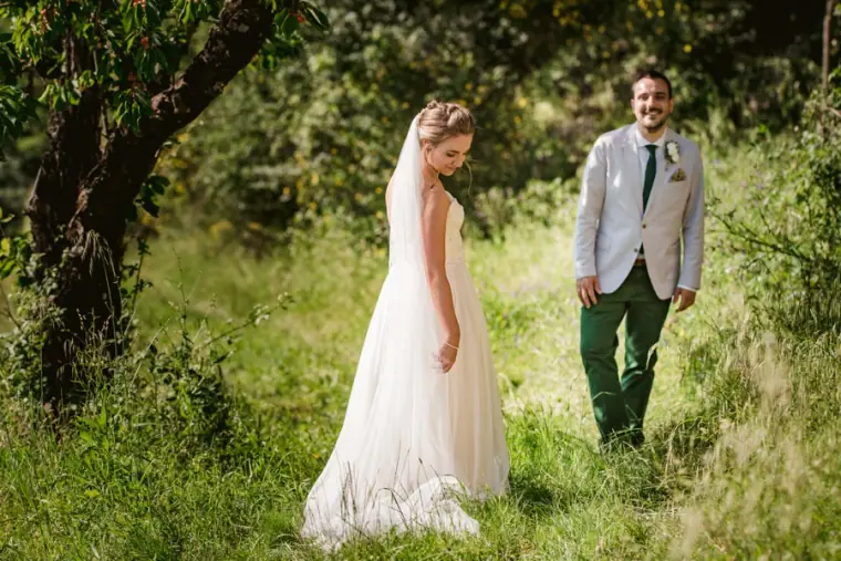 Groom approaching his bride in long grass beneath trees for their first look