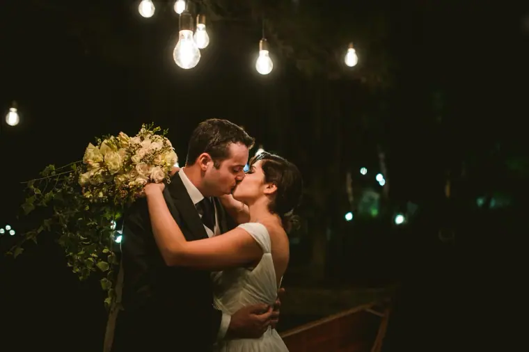Nermine and Chris kissing beneath hanging festoon bulbs at night at Lexeko Estate, Cyprus