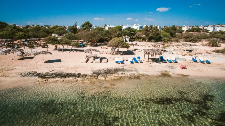Aerial view of the sandy beach and clear shallow water in front of Thalassines Beach Villas