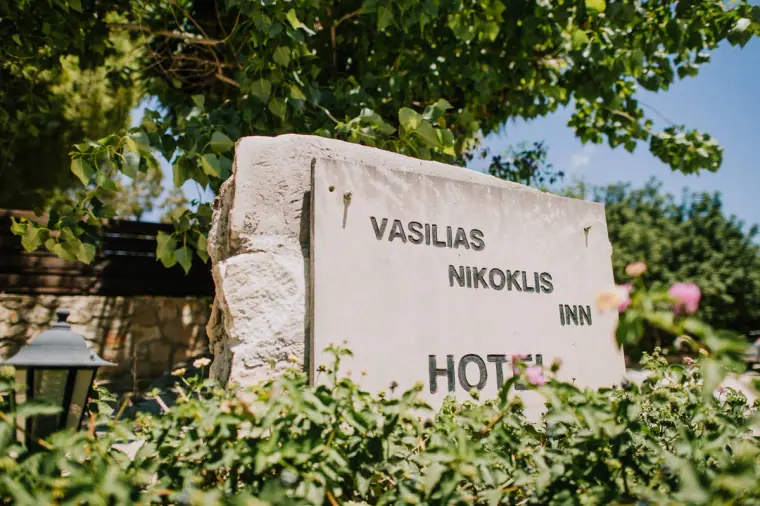 Stone sign for Vasilias Nikoklis Inn surrounded by greenery and roses