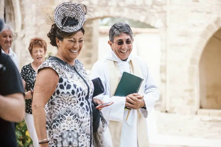 Smiling guest in a feathered fascinator chatting with the priest holding a green book