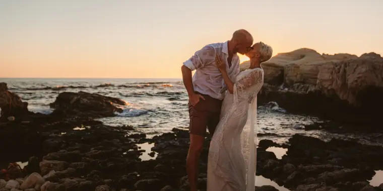 Alana and Luke kissing on the rocks as the sun goes down over the sea near Paphos