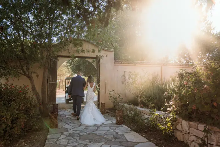 Bride and groom walking through a sunlit garden gateway at Minthis