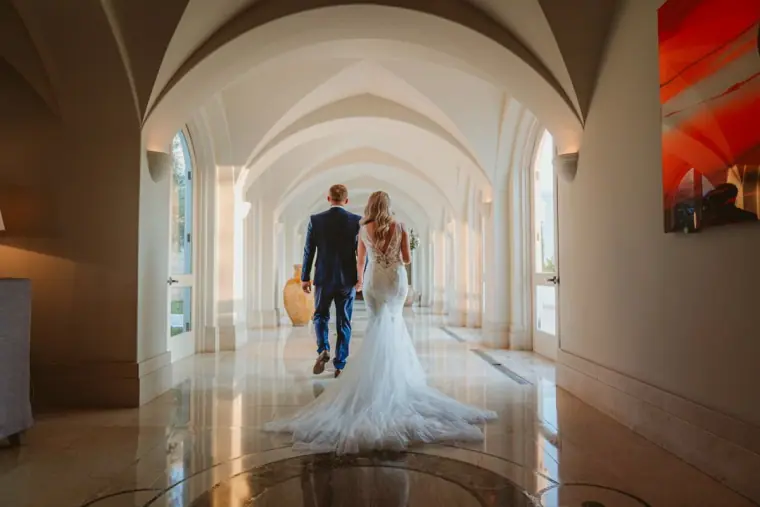 Bride and groom walking away hand in hand through the arched hallway at Anassa Hotel