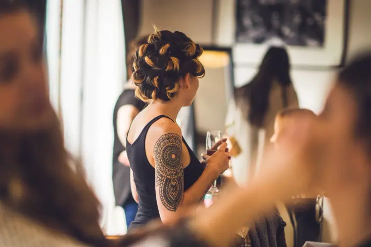 Tattooed bridesmaid in rollers holding a drink as others get ready