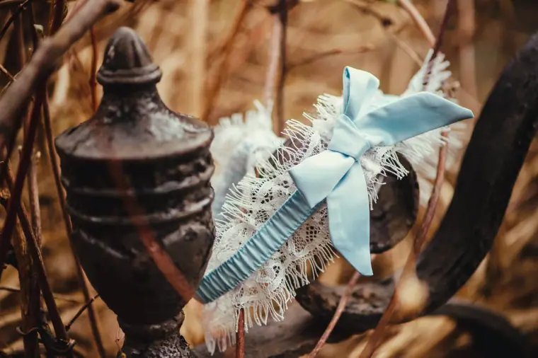 Lace garter with a pale blue bow draped on a dark urn among twigs
