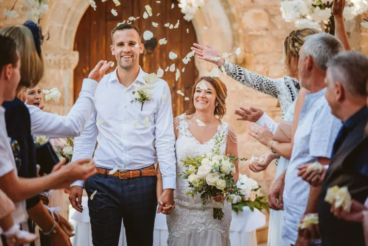 Bride and groom walking through a shower of white petals thrown by guests