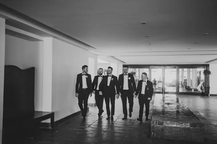 Black-and-white photo of the groomsmen striding down a hotel corridor