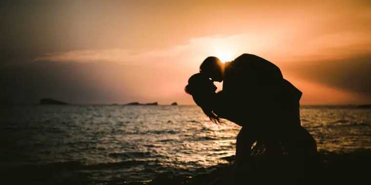 Kenton and Hassiba in silhouette, kissing at the water's edge at sunset, Ibiza