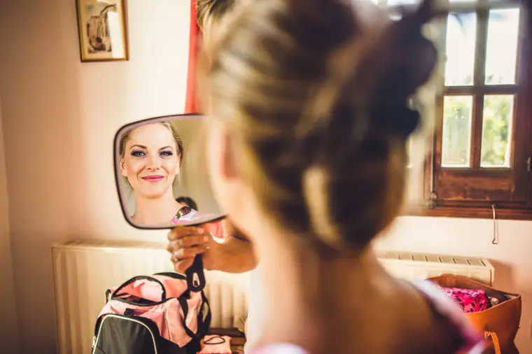 Bride checking her make-up in a hand mirror by the window