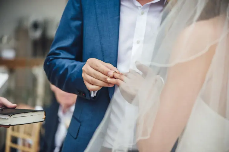 Close-up of the groom placing the ring on the bride's finger beneath her veil