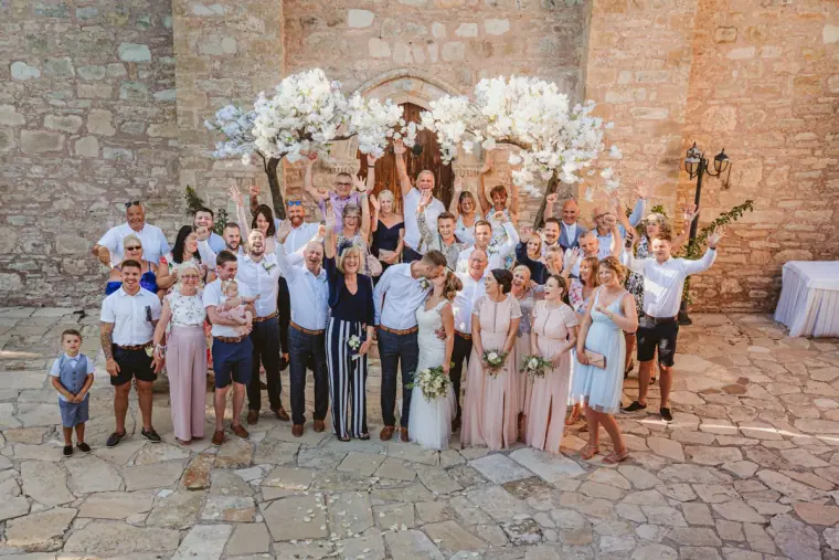 Large group photo of guests cheering in the courtyard in front of the chapel
