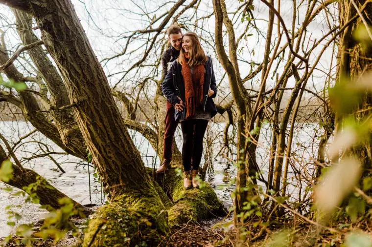 Couple standing on a fallen tree trunk in lakeside woodland