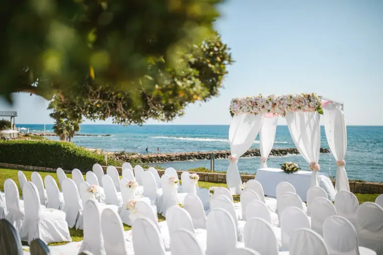 White chairs and a flower-draped canopy set for the ceremony on the seaside lawn at Almyra
