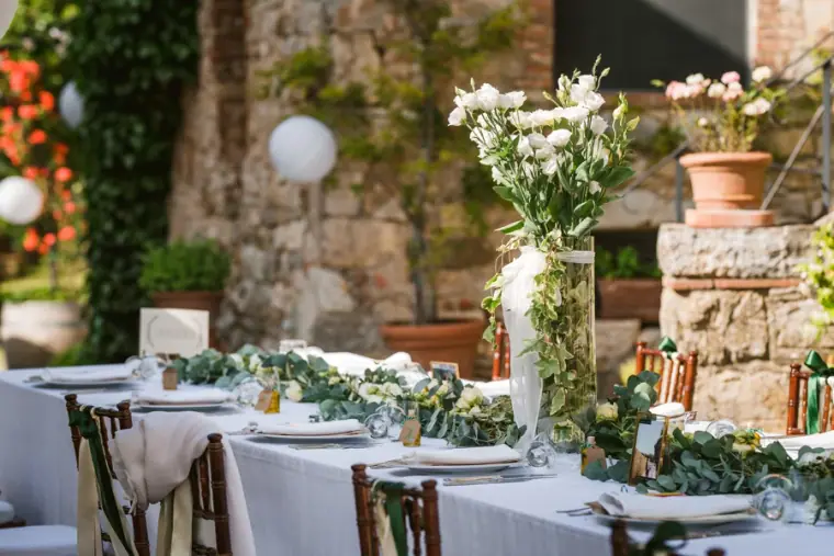 Long reception tables with white linen, eucalyptus garlands and lanterns in a stone courtyard