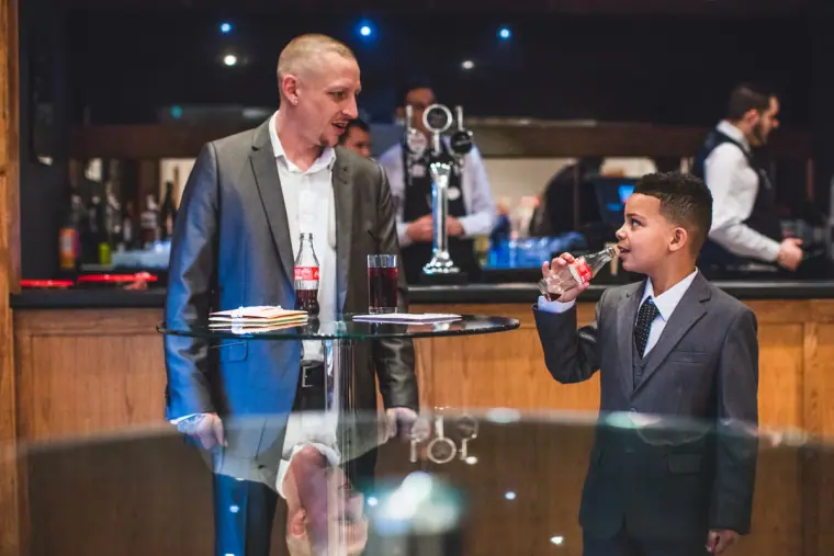Boy in a suit speaking into a microphone at the bar as a man looks on