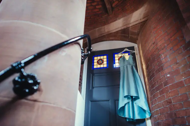 Teal bridesmaid dress hanging from an iron lamp bracket by a red sandstone doorway