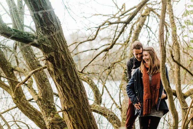 Jana in a red scarf smiling beside Alex among twisted branches