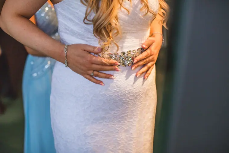 Close-up of the bride's jewelled belt as a bridesmaid in blue stands beside her