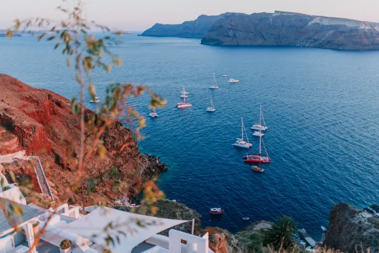 Sailing boats anchored in the deep blue caldera below red cliffs, Santorini