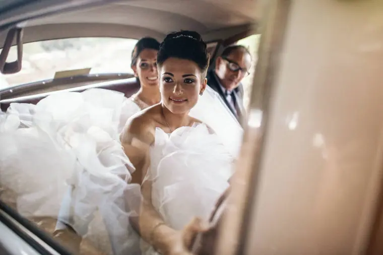 Bride in her veil and tiara smiling from the back seat of the wedding car