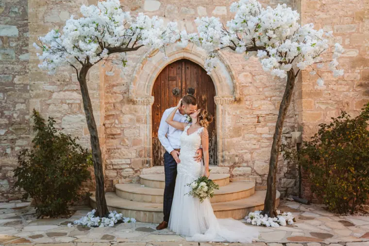 Ellie and Jack kissing on the chapel steps between white blossom trees
