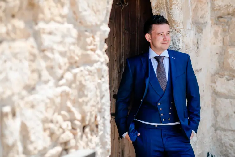 Stephen in a blue three-piece suit leaning in a stone doorway at Ayia Kyriaki