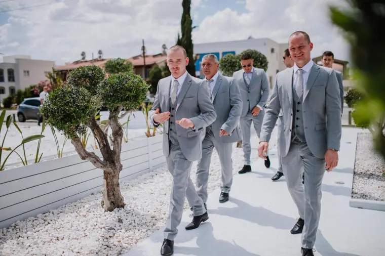 Groom and groomsmen in grey suits walking past olive trees at Galu Seaside