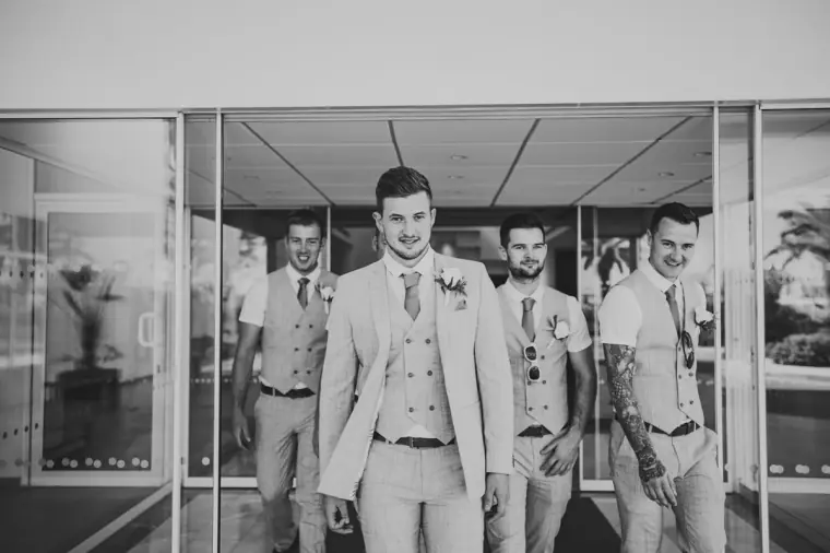 Black-and-white shot of the groom and groomsmen striding through the hotel lobby