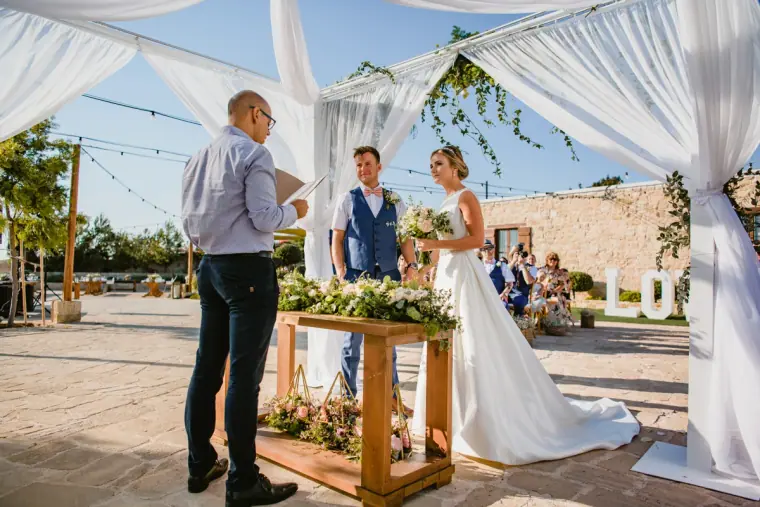 Celebrant leading the ceremony under a white draped arch with the couple