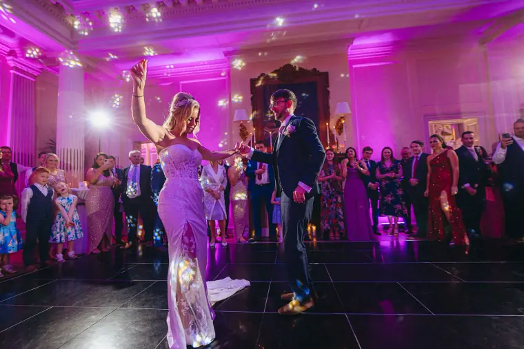 Ian and Jade's first dance as guests watch under pink and purple lighting