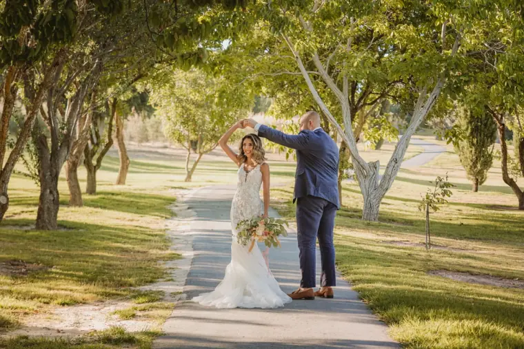 Groom twirling the bride along an olive-tree avenue