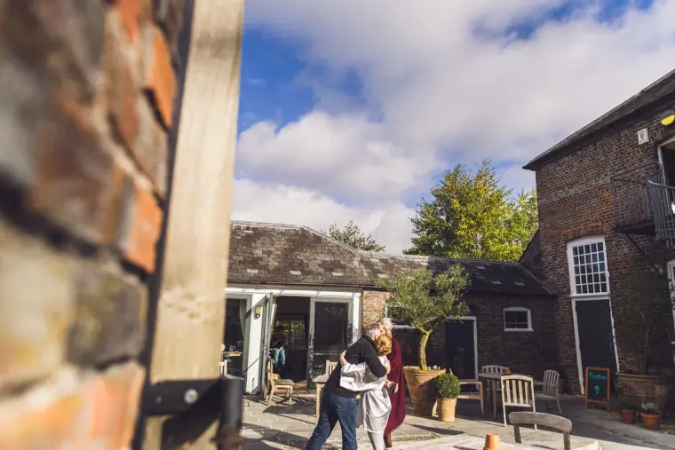 Two people hugging in the sunny courtyard outside The Mews, Wasing Park