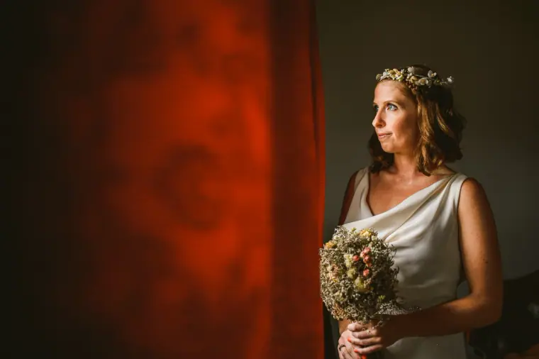 Fleur holding a dried-flower bouquet in soft window light beside a red curtain