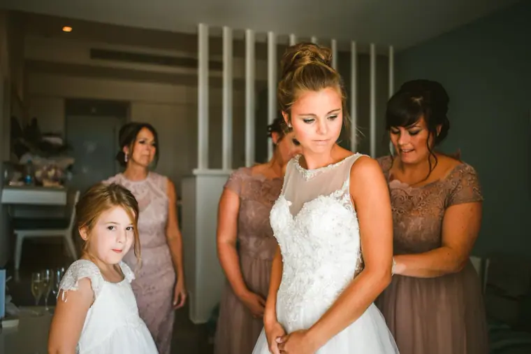 Bridesmaids in blush lace and a flower girl helping the bride into her dress