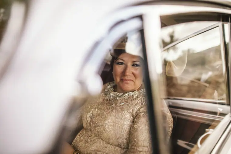 Woman in a gold lace dress glancing out of the wedding car window