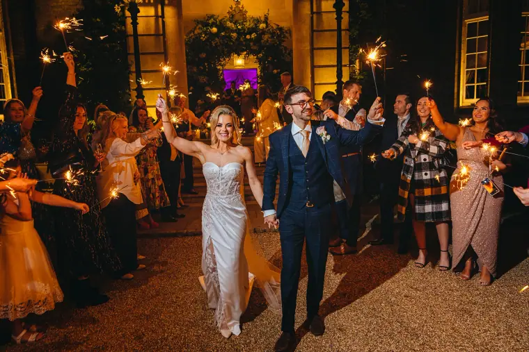 Ian and Jade walking through a tunnel of guests holding sparklers