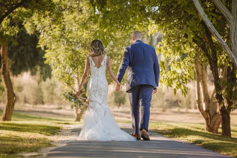 Bride and groom walking away hand in hand down a tree-lined path
