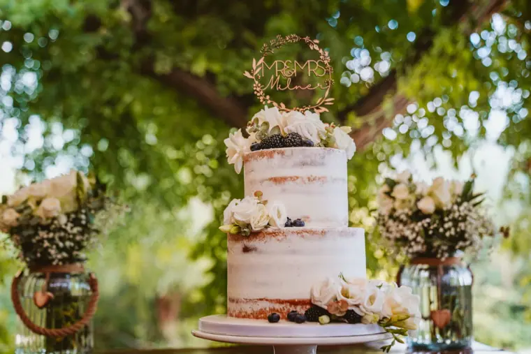 Semi-naked wedding cake with white flowers and a gold monogram topper